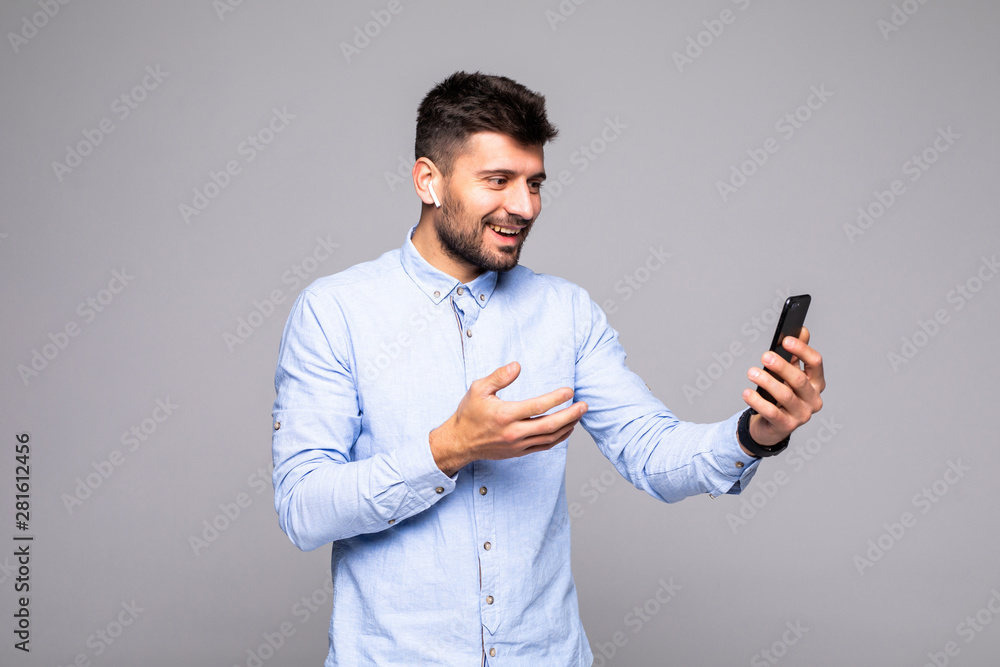 Happy smiling man watching funny video on mobile phone gadget while standing isolated on gray background Happy smiling man watching funny video on mobile phone gadget while standing isolated on gray background