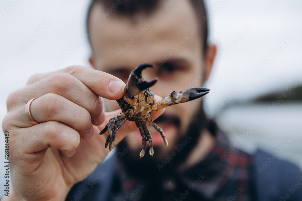 A cool picture of a man who holds a small crab in his arms while walking along the sea in cloudy cold weather