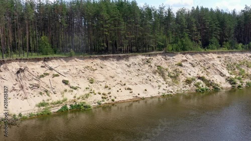 High sandy bank of the picturesque river with green coniferous forest on a sunny summer day