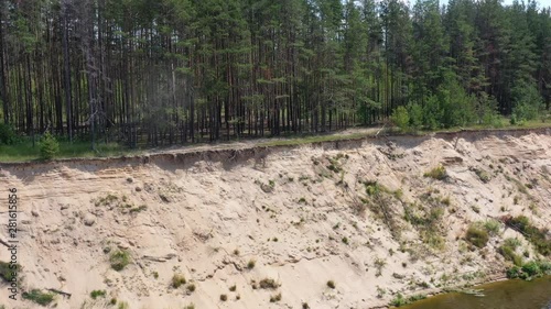 High sandy bank of the picturesque river with green coniferous forest on a sunny summer day