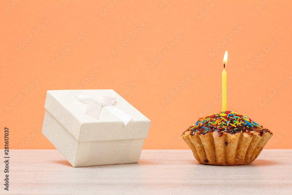 Tasty birthday muffin with burning festive candle and gift box on peach background. Tasty birthday muffin with burning festive candle and gift box on peach background.