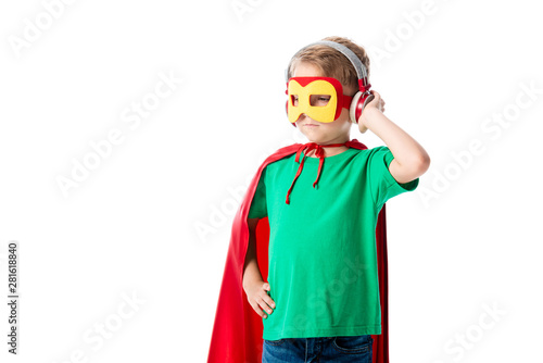 preschooler boy in red hero cloak and mask listening music in headphones and looking away isolated on white