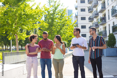 People with gadgets standing and chatting outside. Men and women standing outdoors, holding smartphones and tablet and talking to each other. Wireless technology concept