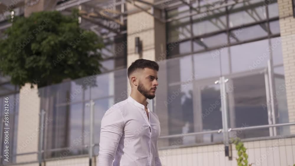 Successful atractive young man walking near big building, businessman looking forward. With big bag full of money. Medium shot Successful atractive young man walking near big building, businessman looking forward. With big bag full of money. Medium shot