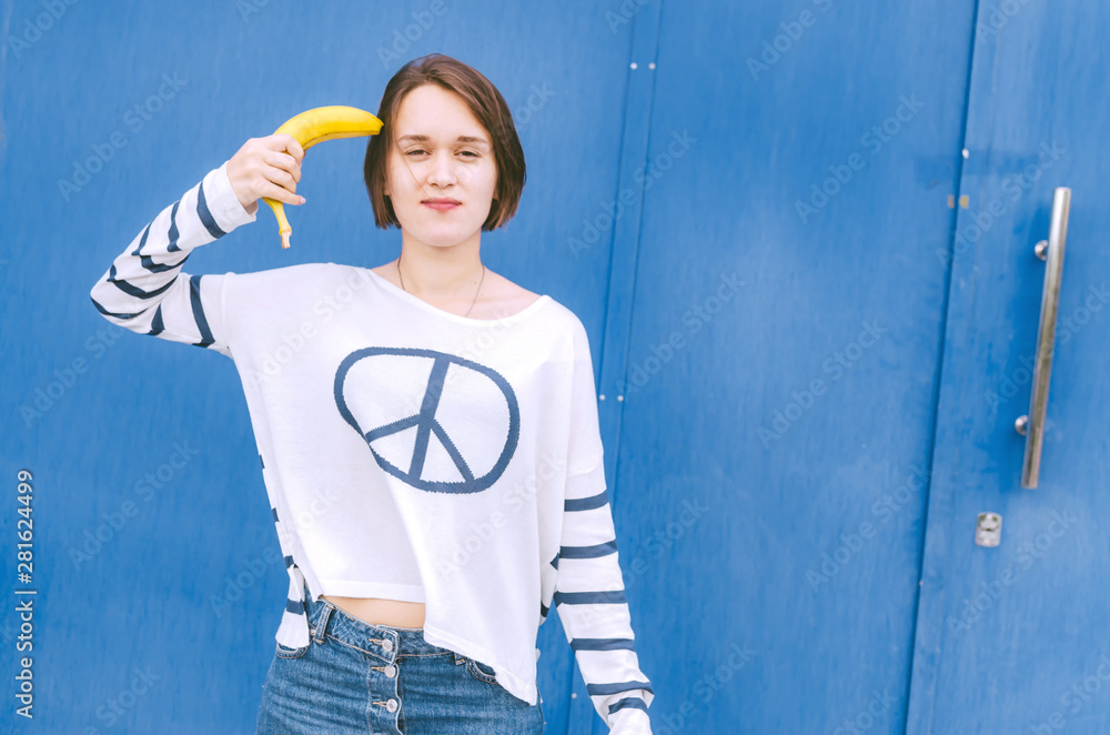 Young adult female with banana staying on blue wall Young adult female with banana staying on blue wall
