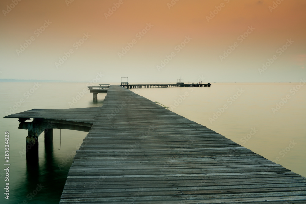Obraz premium Wooden bridge that stretches into the sea at sunrise.
