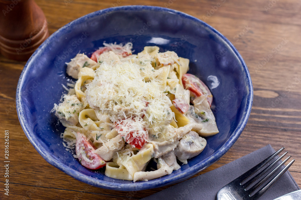 Pasta fettuccine with mushrooms, tomatoes and fried chicken ham in creamy cheese sauce on wooden background. Healthy, tasty food. Diet, holidays, recipe concept. Free space for text. Selective focus Pasta fettuccine with mushrooms, tomatoes and fried chicken ham in creamy cheese sauce on wooden background. Healthy, tasty food. Diet, holidays, recipe concept. Free space for text. Selective focus