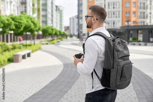 Young man walking with backpack and coffee cup in city.