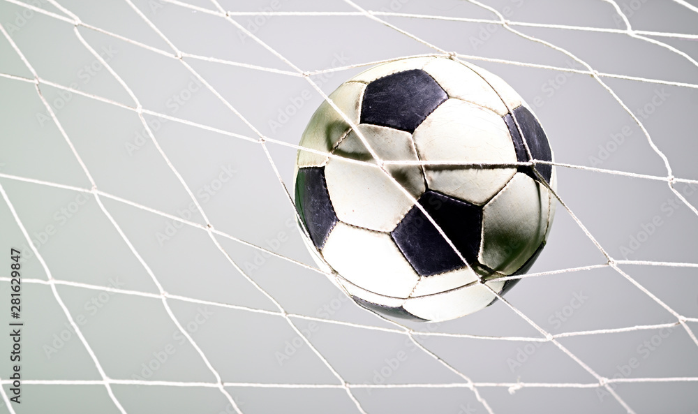 Naklejka premium Scoring goal, Soccer ball in the net against gray background.