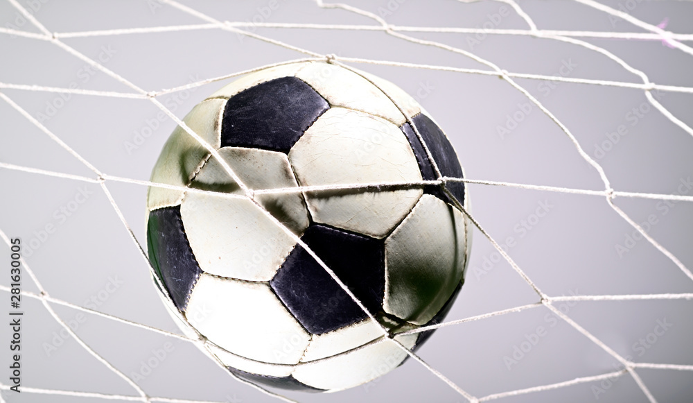 Naklejka premium Scoring goal, Soccer ball in the net against gray background.