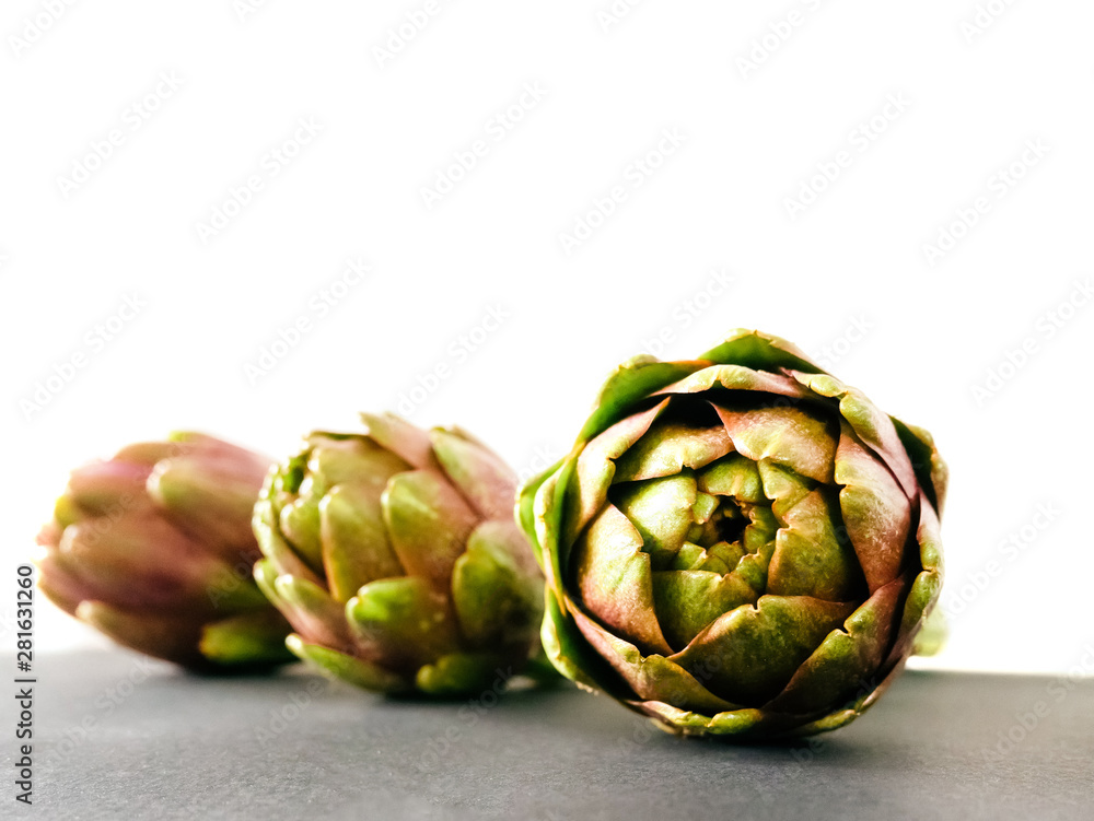 Artichokes on grey background. Fresh organic artichoke flowers with front view Artichokes on grey background. Fresh organic artichoke flowers with front view