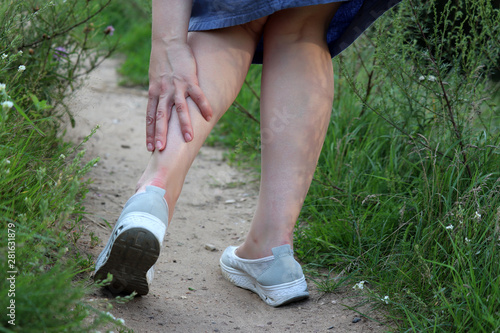 Foot pain, ankle sprain, woman grabbed her leg while walking on a green grass. Concept of tired legs, injury on running