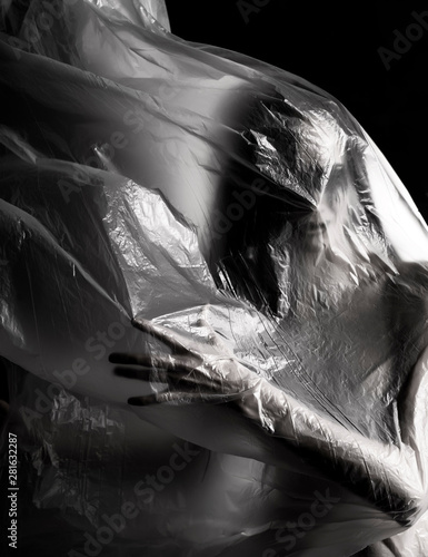 Slim girl dressed only in underwear emotionally posing, wrapped in fluttering in the wind and fitting her graceful young body cellophane film. Artistic, creative, abstract design. Black and white