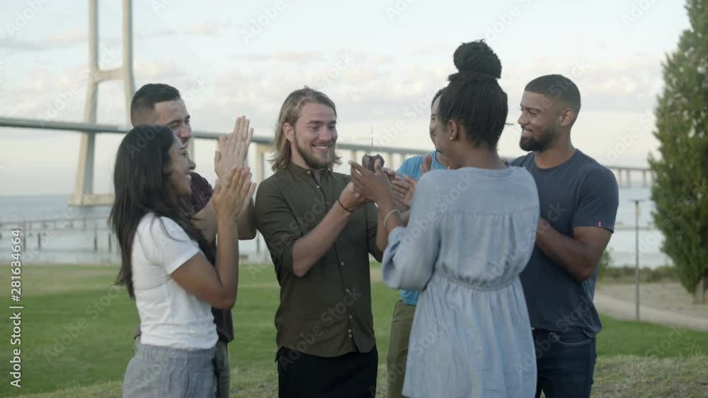 Smiling friends congratulating young bearded man with birthday. Cheerful young people giving muffin with sparkler to handsome guy. Concept of birthday party Smiling friends congratulating young bearded man with birthday. Cheerful young people giving muffin with sparkler to handsome guy. Concept of birthday party