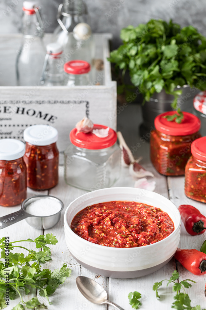 Process of cooking hot sauce of red hot peppers. Ingredients: pepper, greens, basil, paprika on a wooden table. Glass jars with ready-made sauce Process of cooking hot sauce of red hot peppers. Ingredients: pepper, greens, basil, paprika on a wooden table. Glass jars with ready-made sauce