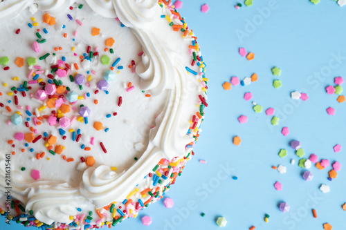 Top View of a cake with white icing and colorful sprinkles on a light blue background