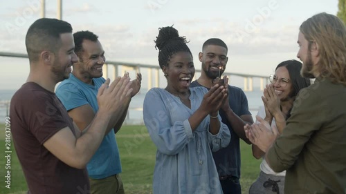 Smiling friends congratulating young woman with birthday. Cheerful young people giving muffin with sparkler. Concept of birthday party
