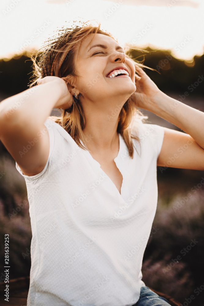 Portrait of a lovely caucasian woman laughing with closed eyes holding a wreath of flower on her head against sunset.