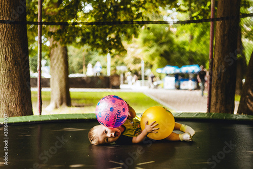 happy and smiling two-year-old boy playing with two balls on a trampoline in the park in summer while walking with his family