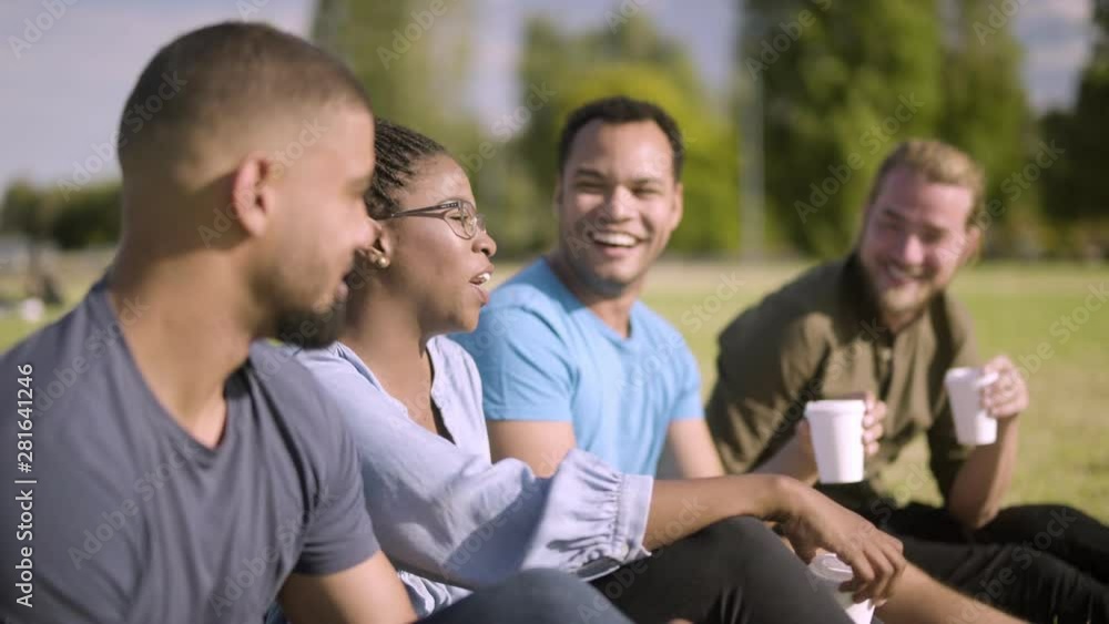 Smiling colleagues sitting on lawn and drinking coffee. Cheerful young people having lively conversation during coffee break. Communication concept Smiling colleagues sitting on lawn and drinking coffee. Cheerful young people having lively conversation during coffee break. Communication concept