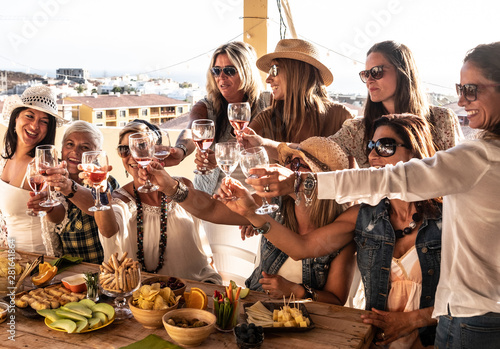 Beautiful women in group celebrate the friendship with some wine glass. Nine caucasian people enjoying the sunset with aperitif