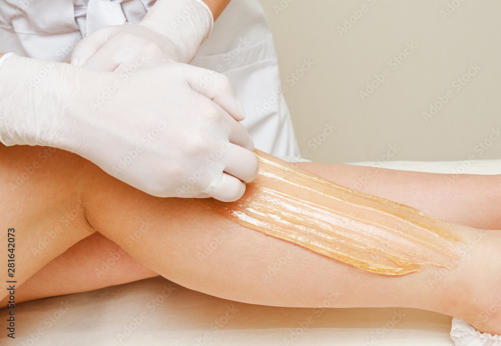 Naklejka premium Cosmetologist beautician waxing female legs in the spa center beauty salon