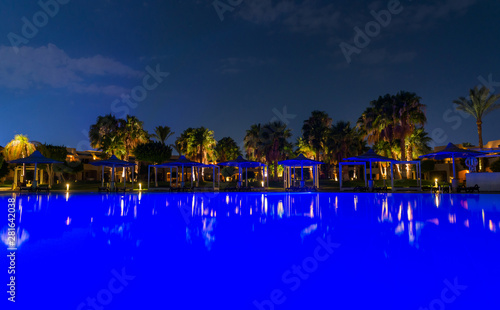 reflections from palm trees and buildings lights over calm pool water surface