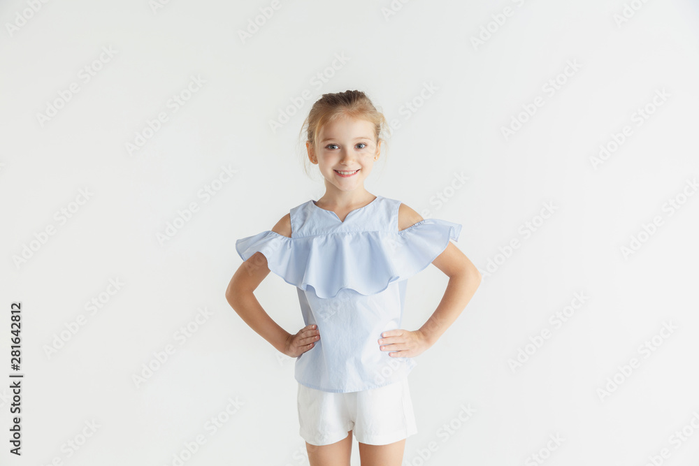 Stylish little smiling girl posing in casual clothes isolated on white studio background. Caucasian blonde female model. Human emotions, facial expression, childhood. Smiling, holding hands on hips. Stylish little smiling girl posing in casual clothes isolated on white studio background. Caucasian blonde female model. Human emotions, facial expression, childhood. Smiling, holding hands on hips.