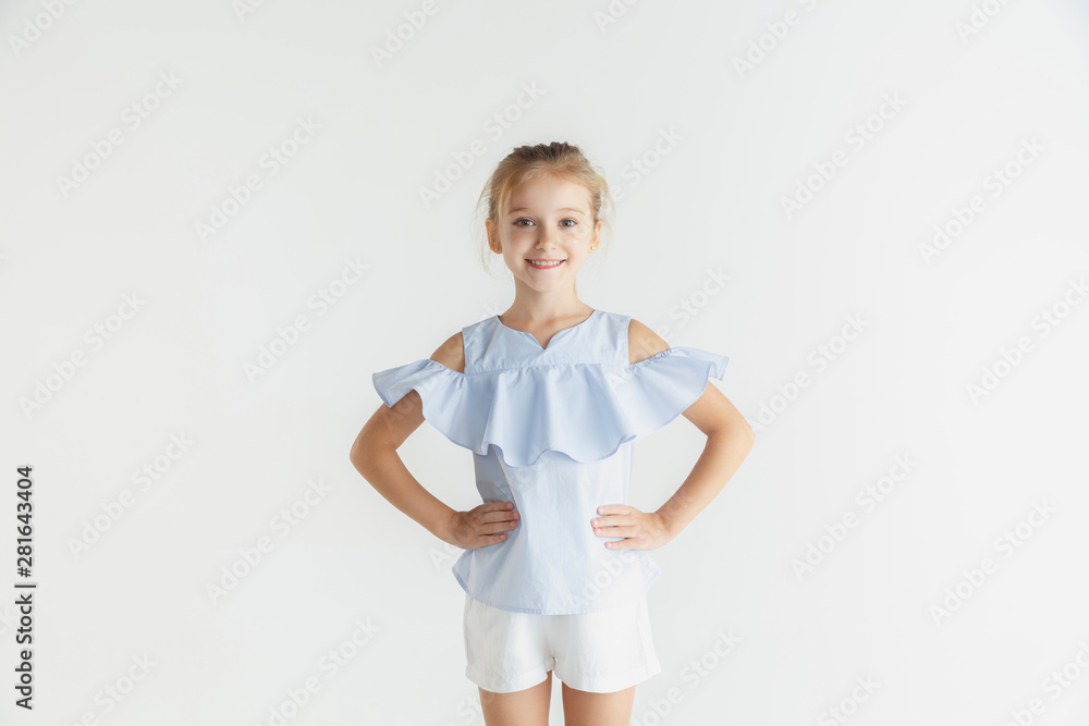 Stylish little smiling girl posing in casual clothes isolated on white studio background. Caucasian blonde female model. Human emotions, facial expression, childhood. Smiling, holding hands on hips. Stylish little smiling girl posing in casual clothes isolated on white studio background. Caucasian blonde female model. Human emotions, facial expression, childhood. Smiling, holding hands on hips.