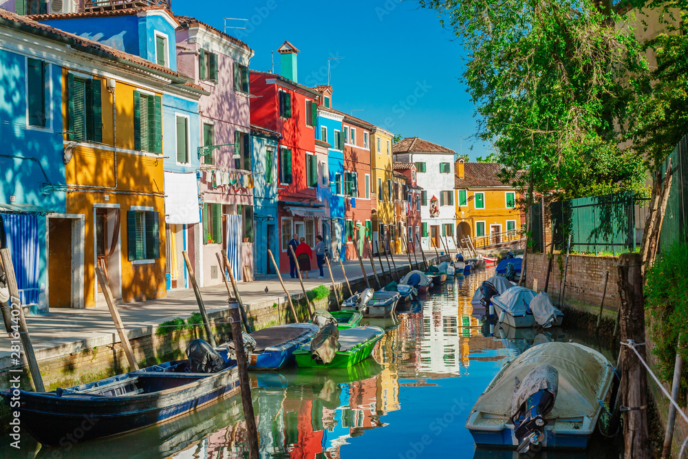 Colorful vibrant houses along a green canal with old boats in Burano Italy