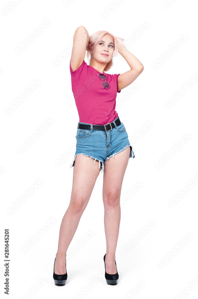 Young happy smiling girl in denim shorts and a pink t-shirt stands in high heels. Isolated on white background. Young happy smiling girl in denim shorts and a pink t-shirt stands in high heels. Isolated on white background.