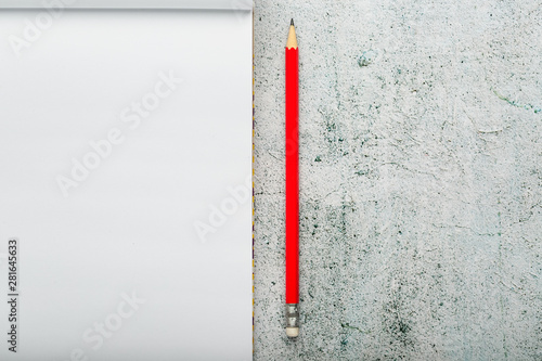 Notepad with a red pencil on a light background for writing. Free empty space for writing on a blank sheet of a notebook.