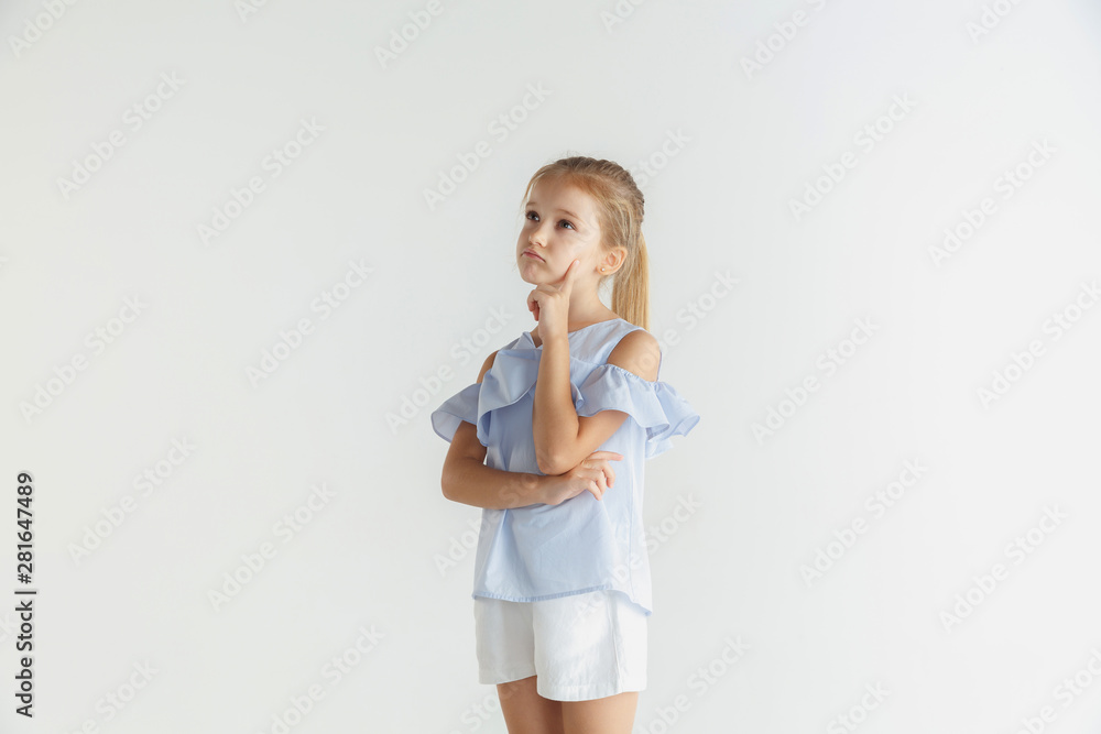 Stylish little smiling girl posing in casual clothes isolated on white studio background. Caucasian blonde female model. Human emotions, facial expression, childhood. Thoughtful. Thinking, choosing. Stylish little smiling girl posing in casual clothes isolated on white studio background. Caucasian blonde female model. Human emotions, facial expression, childhood. Thoughtful. Thinking, choosing.