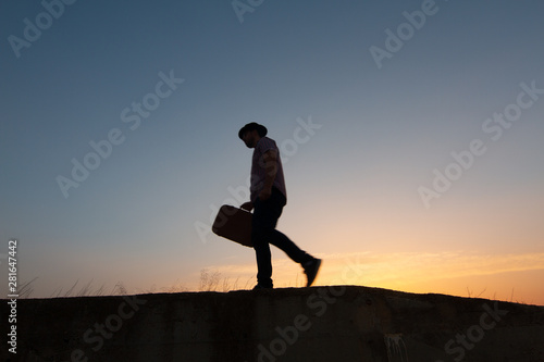 Fototapeta Naklejka Na Ścianę i Meble -  silhouette of man with suitcase at sunrise
