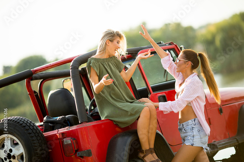 Two young women having fun on hood of a car by the lake © BGStock72