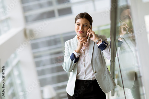 Pretty young business woman stands on the stairs at the office and use mobile phone