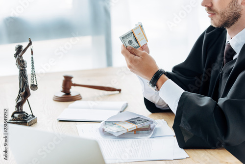 cropped view of judge with clenched hands near money in envelope and wooden gavel