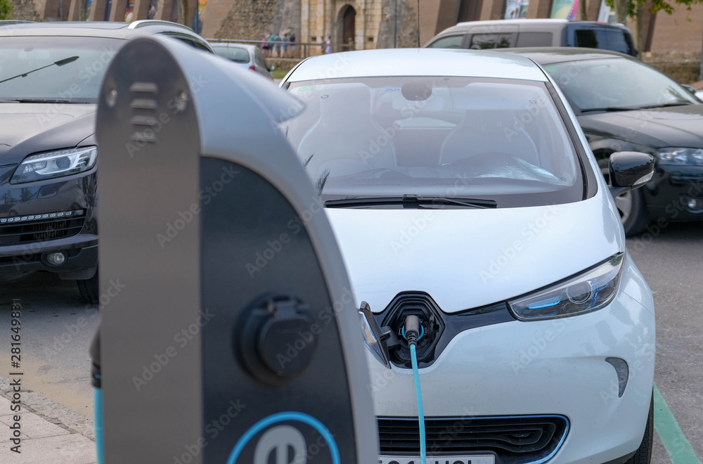Close up of white Electric car at charging station with power cable supply plugged. Eco-friendly alternative energy concept. Power supply connect to electric vehicle. Front view. Chip electric cars.