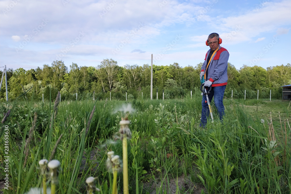 The headphone and glasses worker mows the grass in the field.