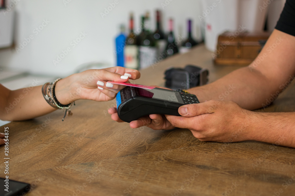 A young woman pays with credit card in a pub. The waiter holds a credit card terminal. Close up A young woman pays with credit card in a pub. The waiter holds a credit card terminal. Close up
