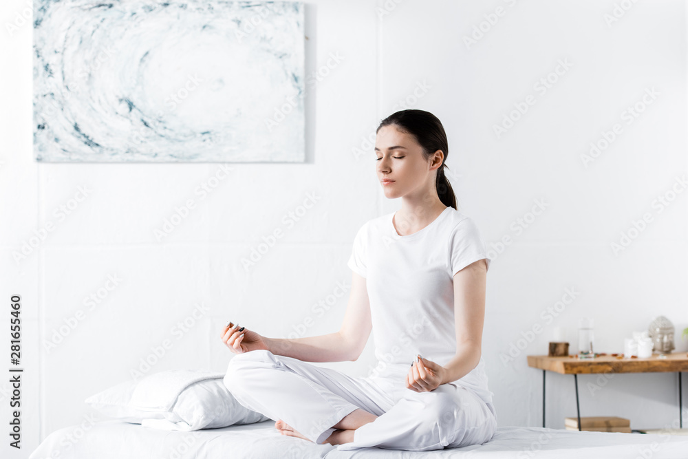 woman sitting on massage table in lotus pose with closed eyes woman sitting on massage table in lotus pose with closed eyes