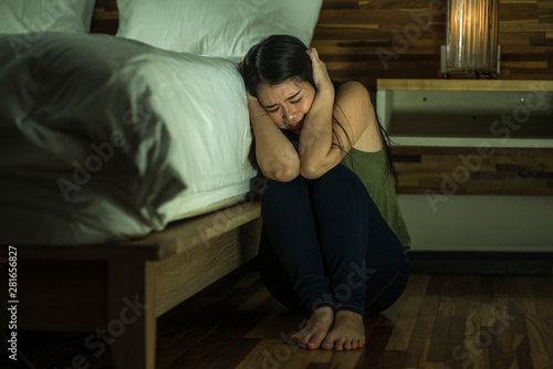 dramatic lifestyle portrait of young depressed and sad Asian Chinese woman sitting on floor at bedroom next to bed suffering depression problem and anxiety crisis