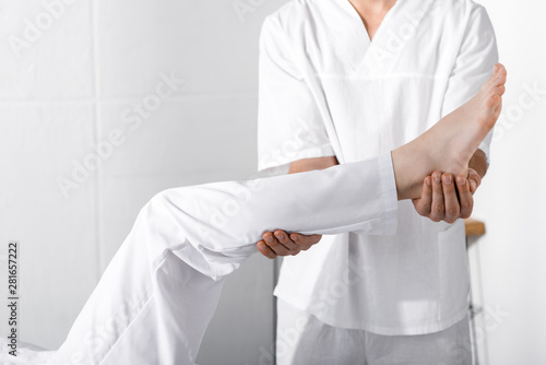cropped view of masseur standing near woman and touching her leg