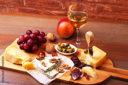 Assortment of cheese with fruits, grapes, nuts and cheese knife on a wooden serving tray. photo