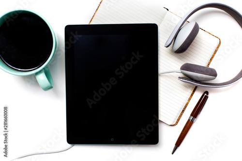 Blank screen tablet/iPad device on white background with headphones, coffee, open notebook, and pen