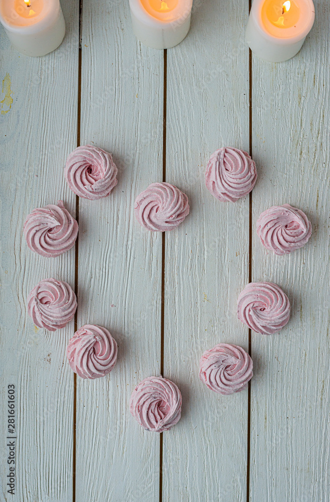 Zephyr lined in a heart shape with burning candles on a white background. Flat lay. Top view. Pink sweet homemade zephyr or marshmallow. Colorful meringues on white. top view dessert image. Zephyr lined in a heart shape with burning candles on a white background. Flat lay. Top view. Pink sweet homemade zephyr or marshmallow. Colorful meringues on white. top view dessert image.