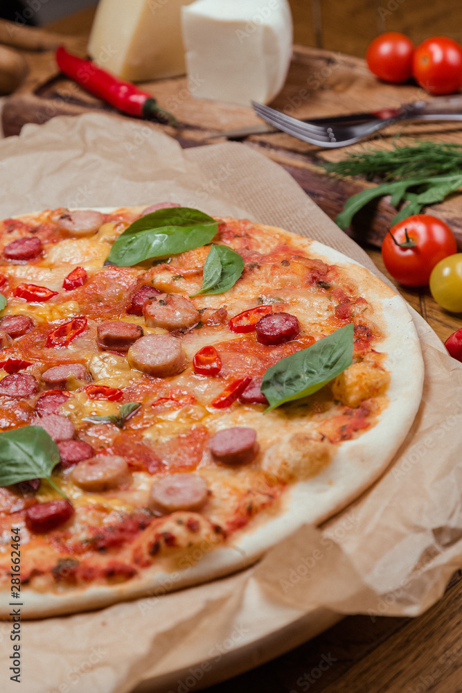 italian pizza with assorted sausages and hot pepper, the background is decorated with vegetables, on a wooden background italian pizza with assorted sausages and hot pepper, the background is decorated with vegetables, on a wooden background