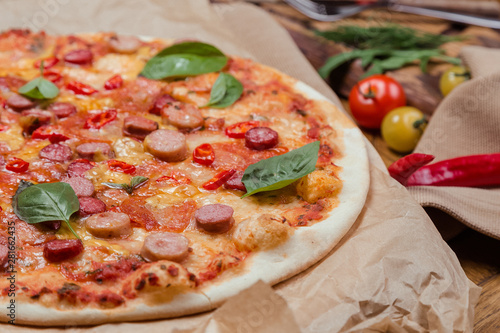 italian pizza with assorted sausages and hot pepper, the background is decorated with vegetables, on a wooden background