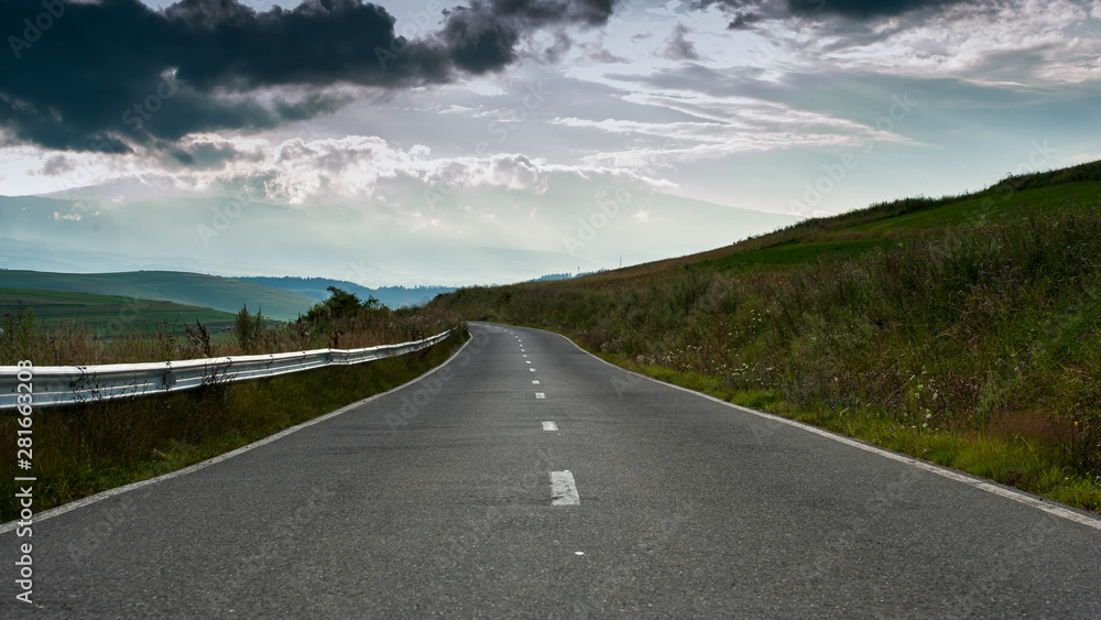 Fototapeta premium Empty rural asphalt road with green vegetation, clearing sky after summer rainstorm.