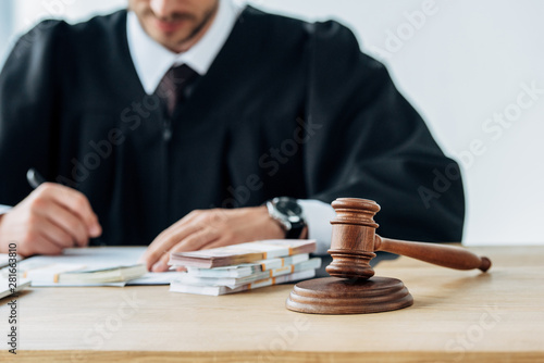 selective focus of gavel near judge holding dollar banknotes in office